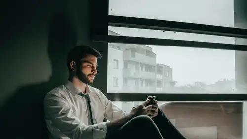 A man sitting by a window, reading messages on his phone